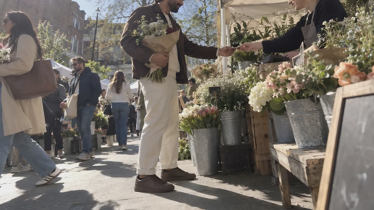 A man in chocolate TREAD Court sneakers buying flowers at a market stall