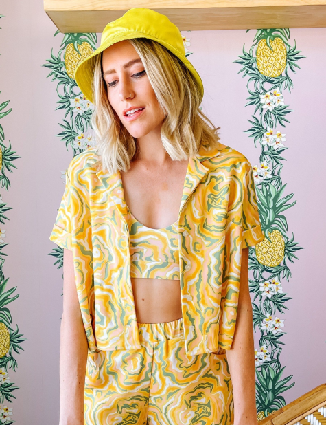 A woman wearing a yellow short sleeve shirt with a green and orange abstract print on it.