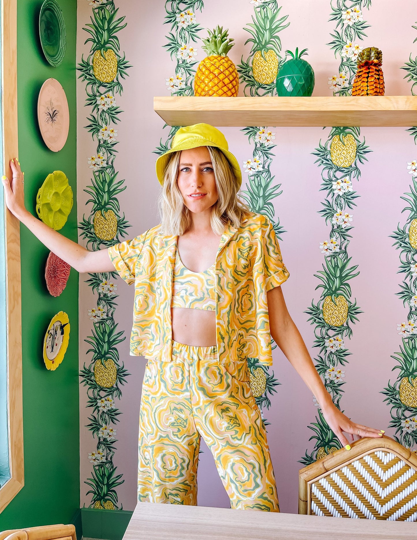 A woman wearing a yellow short sleeve shirt with a green and orange abstract print on it.